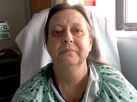View of Elizabeth sitting independently in a chair in her hospital room.