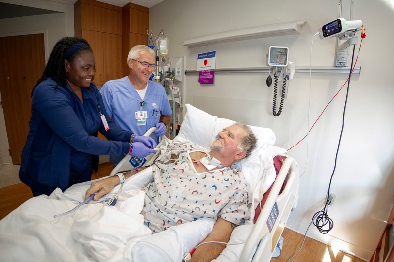A male patient lays in a hospital bed as his care team takes care of him.